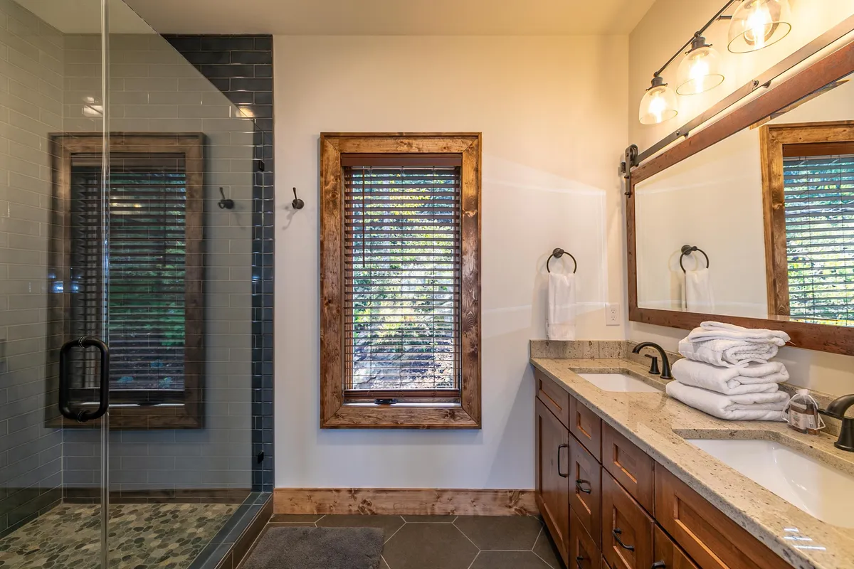 A bright and refreshing bathroom featuring a spacious shower area, a modern double sink vanity with mirrors, and abundant natural light streaming through a window. The clean lines and fresh ambiance evoke a spa-like setting ideal for self-care.