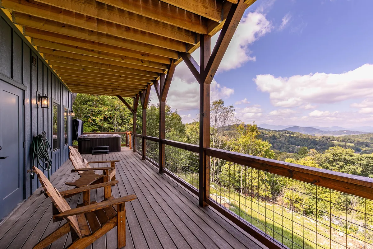This photo captures the lower level deck featuring a bubbling hot tub framed by sturdy wooden railings. Adirondack chairs are arranged around the tub, with a dramatic mountain view beyond. The scene is set during the golden hour, highlighting the tranquil mood and inviting ambiance perfect for soaking under the stars or relaxing after a day of exploration.