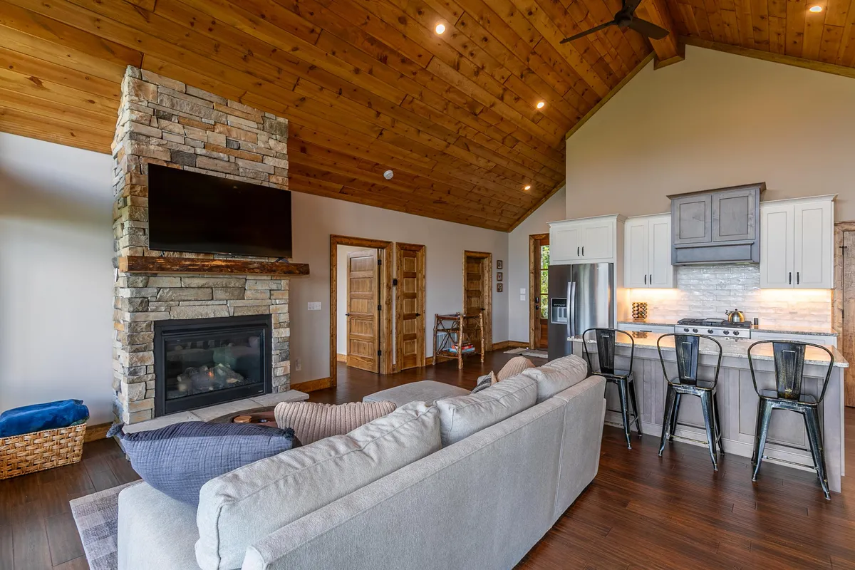 This interior shot highlights the seamless flow between the stone fireplace, the large sectional sofa, and the open kitchen area with a prominent island. The warm lighting and use of natural materials emphasize the inviting, communal nature of the space, ideal for both relaxation and entertaining.