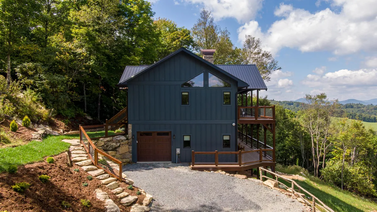 A wide exterior view of the home's modern architecture, deck area, and surrounding greenery, with mountain views stretching into the distance. The inviting deck space encourages gatherings or private moments to take in the natural scenery.
