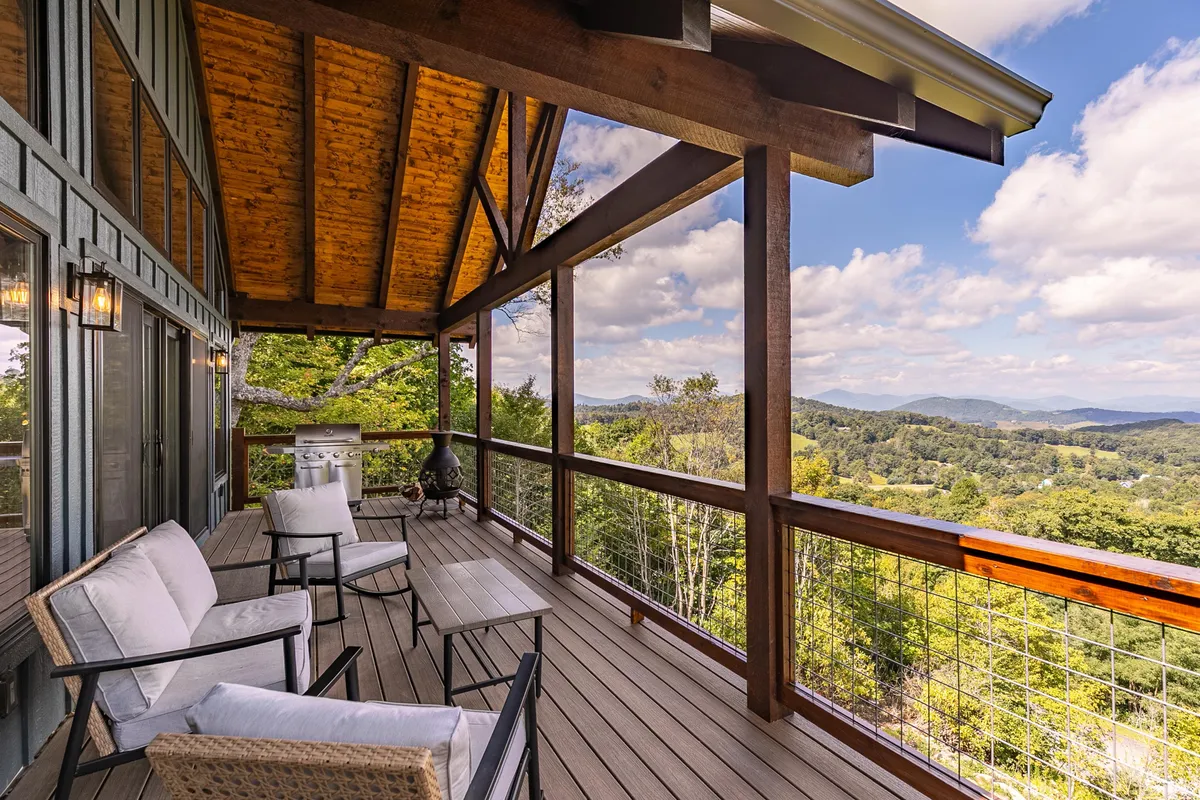 A broad perspective of the main deck highlights plush seating, a convenient outdoor grill, and a sweeping view of rolling mountains. The seating area is set up for relaxation or sharing a meal, with the natural surroundings creating a seamless indoor-outdoor living experience. Soft evening light enhances the tranquil mood.