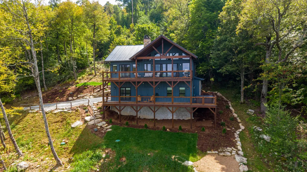 A welcoming exterior shot showcasing the house nestled among trees, featuring a landscaped yard, decks, and broad views. The environment evokes serenity and provides a sense of arrival and connection to nature, ideal for family barbecues or morning coffee outdoors.