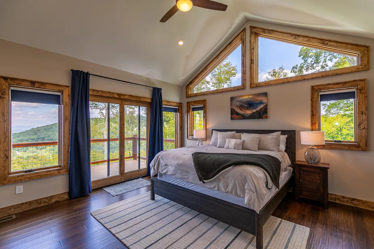A calm and peaceful bedroom featuring a comfortable bed with layered bedding, stylish nightstands with lamps, and large windows offering scenic views. The soft natural light and cozy decor create a restful retreat, perfect for relaxing with a book or enjoying the quiet mountain scenery.