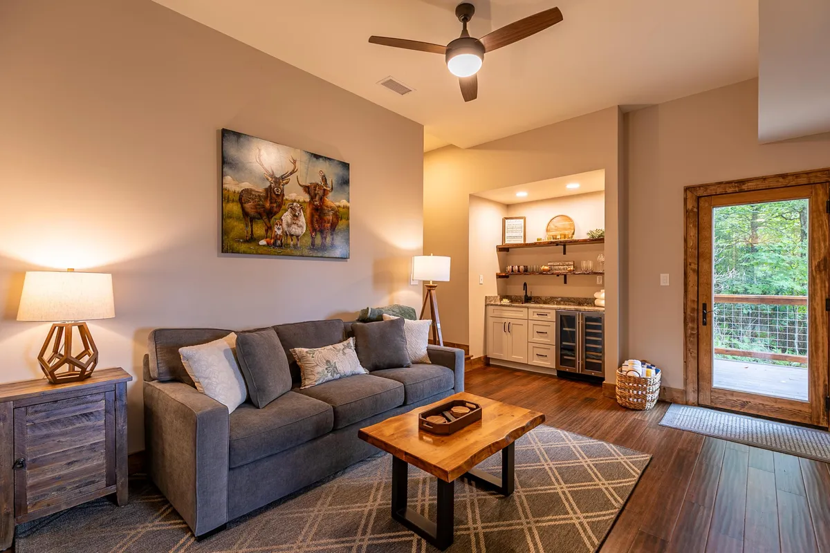 A comfortable living space with a plush sofa, coffee table, stylish artwork, and a window providing natural light. A lamp in the corner and an open doorway add to the welcoming feel of the room.