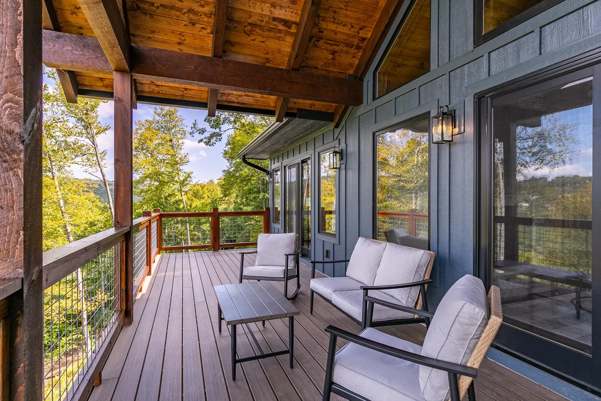 This exterior image features inviting outdoor seating beneath wooden beams and glass doors, with a scenic landscape view beyond. The setting is tranquil and designed for relaxation, socializing, and enjoying the natural mountain surroundings, with hints of seasonal beauty such as autumn foliage and opportunities for sunrise or stargazing.